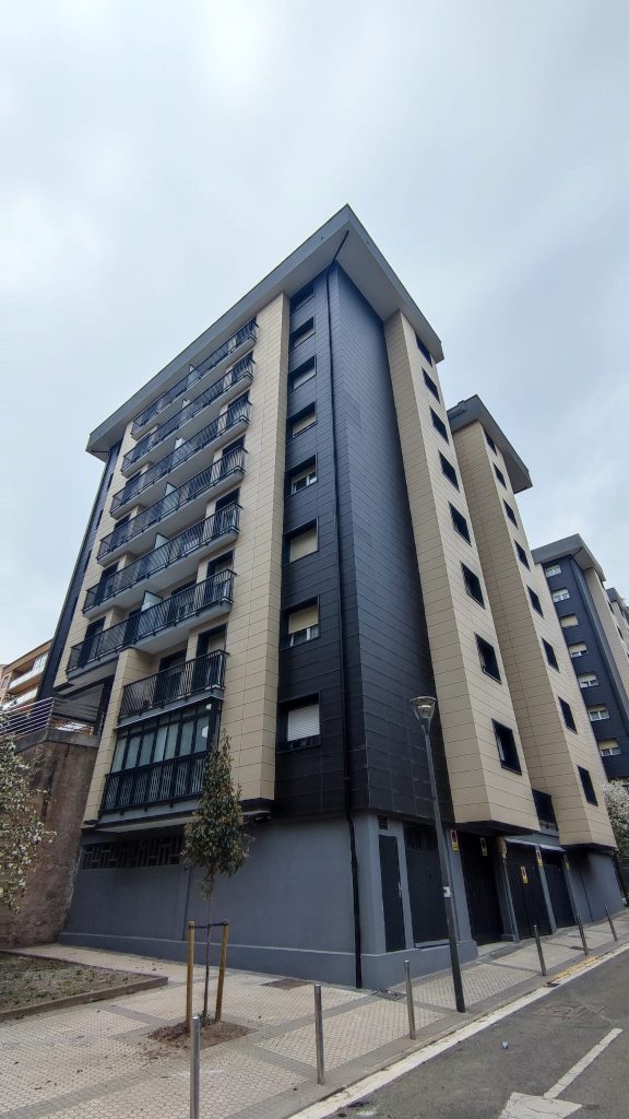 Edificio residencial de gran altura rehabilitado en Gipuzkoa, con fachada ventilada en tonos claros y oscuros y barandillas metálicas.