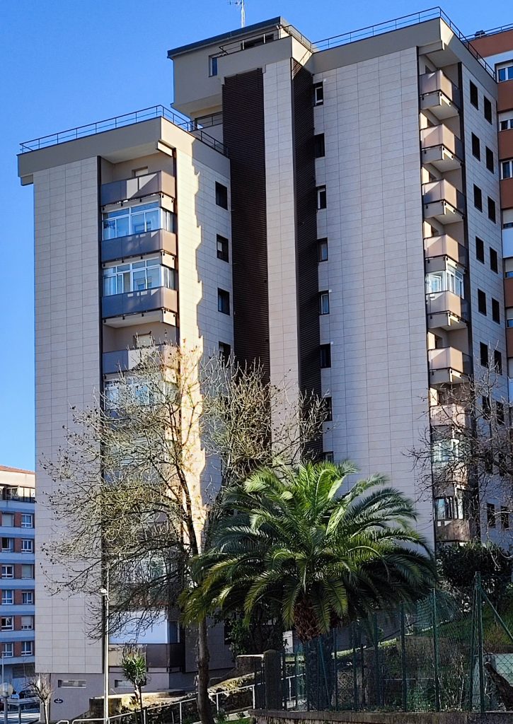 Edificio residencial alto rehabilitado con acabados modernos en Gipuzkoa, rodeado de árboles y cielo despejado.